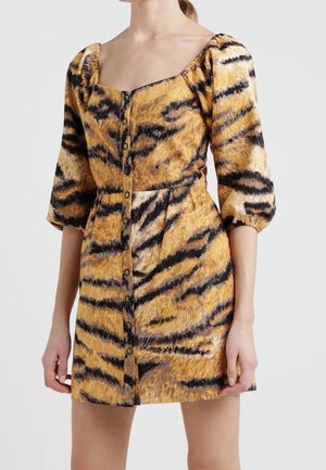 Woman wearing a short, buttoned dress with puffed three-quarter sleeves and a yellow, black, and beige tiger-stripe pattern.