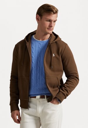 Brown zip-up hoodie with a kangaroo pocket, paired with a blue cable-knit sweater. Features drawstrings and a small logo on the chest.