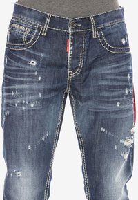 Blaue Jeans aus Denim mit distressed Details, leichter Ausbleichung und kontrastierenden weißen Nähten. Enthält einen Metallknopf und zwei Fronttaschen.