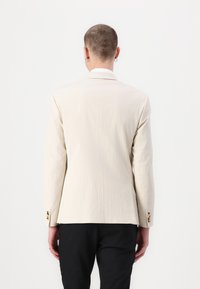 Lichtbeige blazer met een gestructureerde afwerking, enkele knoopsluiting en gouden accenten op de mouwen. Getailleerde pasvorm met lange mouwen.