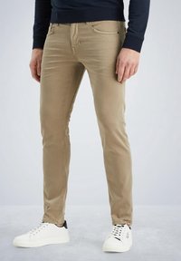 Chinos slim-fit de algodón color caqui con un acabado desgastado, diseño de cinco bolsillos y costuras en contraste. Combinados con zapatillas deportivas blancas de perfil bajo.