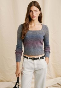 Graues und lila Ombre-Strickpullover mit quadratischem Ausschnitt, gerippten Bündchen und tailliertem Schnitt, kombiniert mit hoch taillierten weißen Hosen und einem schwarzen Gürtel.