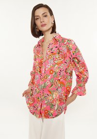 Camicia a maniche lunghe con pattern floreale in rosa, caratterizzata da vivaci dettagli arancioni e verdi, maniche lunghe con polsini arricciati e una vestibilità ampia.