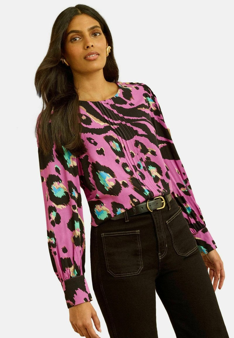 Lilla ja musta pikad varrukad leopardimustriga, türkiissiniste ja roheliste aktsentidega, kokku sobitatud kõrge vöökohaga mustade teksadega.