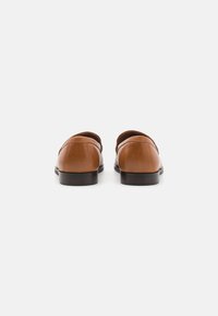 Bruine leren loafers met een gladde textuur, ronde neus en platte zool. Eenvoudige stiksel details langs de randen en een iets verhoogde hak.