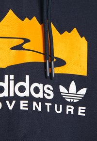 Námořnický svetr s oranžovou grafikou hory a bílým logem "adidas ADVENTURE". Obsahuje černé šňůrky s kovovými koncovkami.