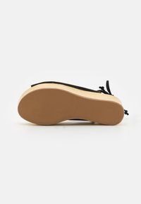 Sandale compensée noire avec semelle en caoutchouc couleur fauve et plateforme en bois, vue par en dessous, montrant la taille indiquée sur la semelle.