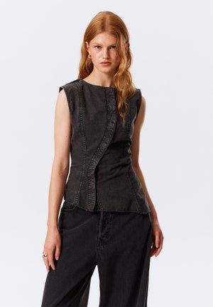 Mouwloze zwarte denim top met een gebogen voornaad, rauwe randen en een aansluitend ontwerp. Gecombineerd met losse zwarte denim broek.