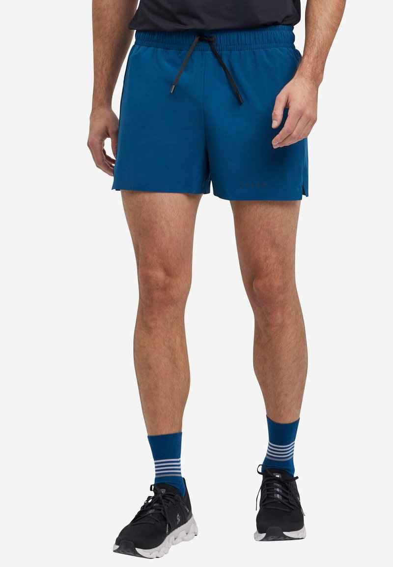 Shorts atletici blu con vita regolabile tramite cordino, aperture laterali e una superficie liscia. Indossati con scarpe nere e calzini a righe blu.