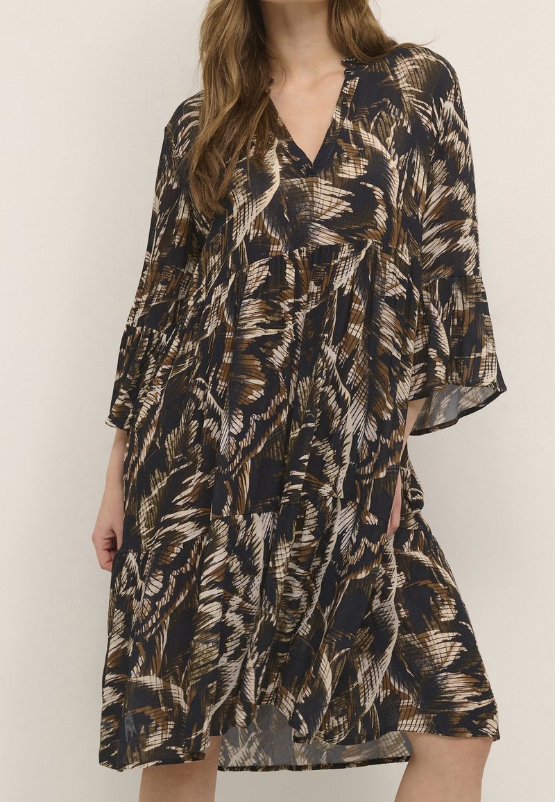 Femme portant une robe ample longueur genou avec un motif abstrait plume foncé et des manches évasées trois-quarts.