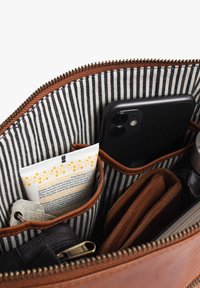 Innenraum einer braunen Ledertasche mit gestreiftem Innenfutter, ausgestattet mit einem Smartphone, Schlüsseln, Portemonnaie und einer Tube Creme in organisierten Fächern.