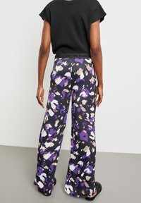 Pantalons larges en tissu noir avec un motif abstrait coloré comprenant du violet, du blanc et du beige. Taille élastique avec un logo.