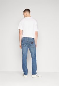 Blugi din denim de culoare albastru deschis cu croi drept, cu buzunare pe spate și un detaliu de pată închisă. Purtați cu un tricou alb simplu și sneakerși.