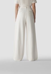 Weite Hosen aus leichtem, cremefarbenem Stoff; mit Gesäßtaschen und glatter Textur. Hochtailliertes Design, maßgeschneiderte Passform an der Taille.