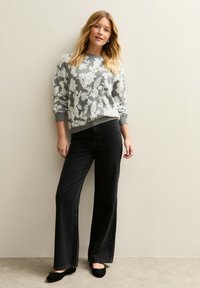 Suéter floral gris claro de punto suave, combinado con jeans negros de pierna ancha y cintura alta, y zapatos planos negros. Texturas suaves y diseño sencillo.