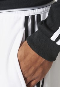 Svartvita sportiga joggers med tre svarta ränder längs sidorna, en ficka med dragkedja och ribbade muddar i strukturerad tyg.