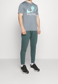 Camiseta gris con un estampado gráfico de un personaje y el texto "Keep Rolling", combinada con pantalones jogger verdes y zapatillas negras.