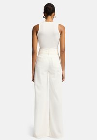 Wit geribbelde tanktop gecombineerd met high-waisted, brede witte broek, met achterzakken en een gladde textuur.