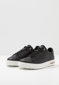 Baskets en cuir noir avec semelle en caoutchouc blanche, dotées d'un bout rond, de lacets fins et d'œillets en métal. Agrémentées d'une bande texturée sur le côté.