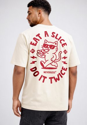 Mann trägt cremefarbenes T-Shirt mit rotem Grafikbild einer Katze mit Sonnenbrille, die ein Stück Pizza hält, und dem Text „Iss ein Stück, mach es zweimal.“