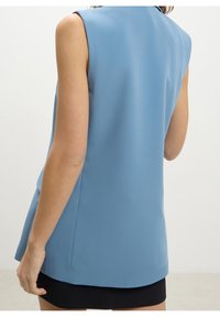 Modrý top bez rukávů s hladkým povrchem, s kulatým výstřihem a mírně rozšířeným lemem. Design je minimalistický.