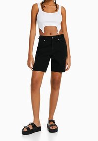 Mustat farkkushortsit, joissa on raaka helma, viisi taskua ja edessä nappikiinnitys. Yhdistetty valkoiseen ribbikangaspaitaan ja mustiin platofrum sandaaleihin.