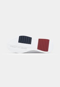 Fehér sneaker talp piros és sötétkék gumis részletekkel, texturált mintázattal és a "TOMMY JEANS" márkanevével a saroknál.