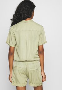 Olivgrön short-sleeve romper med avslappnad passform, elastisk midja och rullade ärmar, med två bakfickor och en slät yta.