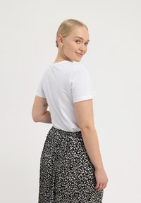 Hvid t-shirt med korte ærmer båret sammen med et sort nederdel med hvidt pletmønster. Glat tekstur, afslappet pasform og rund halsudskæring.