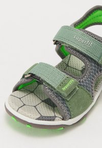 Grön sandal med dubbla remmar, mesh- och mockamaterial, strukturerad sula, hexagonmönster och gröna accenter. Utrustad med justerbara stängningar.
