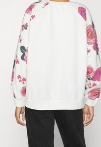 Felpa bianca con motivo floreale rosa e verde sulle maniche, polsini a coste e vestibilità comoda, vista posteriore.