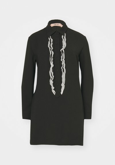 Black dress featuring a collared neckline, long sleeves, and a front placket embellished with zigzag silver trim. Smooth fabric texture.