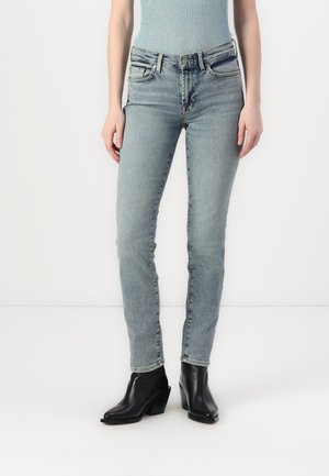 Light blue skinny jeans made of denim, featuring a mid-rise waist, five pockets, and subtle fading. Paired with black heeled ankle boots.