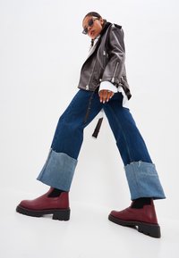 Stivaletti neri con plateau, jeans in denim blu a gamba larga con orli sfilacciati e una giacca da moto in pelle grigia, creando un look stratificato.