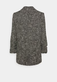 Blazer en tweed noir et blanc avec une finition texturée, doté d'un col, de manches retroussées et d'une silhouette tailleur classique.