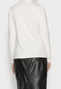 Top a maniche lunghe di un leggero beige con collo alto. Abbinato a una gonna a tubino nera in pelle con tasche posteriori e una trama liscia.