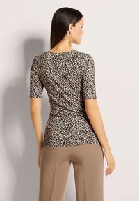 Lässiges leopardprint Oberteil in hellem Beige mit kurzen Ärmeln, das über eine glatte Textur und einen runden Halsausschnitt verfügt, kombiniert mit lockeren beigen Hosen.
