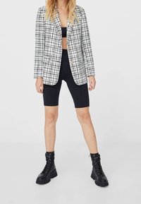 Black and white houndstooth blazer featuring a lapel collar, single button closure, paired with black shorts and chunky black lace-up boots.