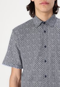 Cămașă cu mânecă scurtă, cu nasturi, în navy și alb, având un model geometric, guler clasic și nasturi negri. Material texturat.