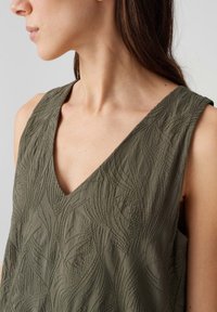 Olive green sleeveless top with a deep V-neck and embossed leaf patterns, featuring textured fabric and a relaxed fit.