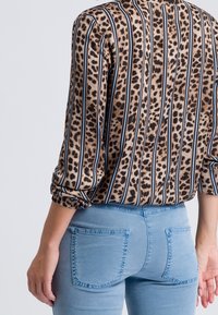 Blouse met luipaardprint en zwart-blauwe verticale strepen, lange mouwen en elastische manchetten, gecombineerd met lichtblauwe high-waisted jeans.