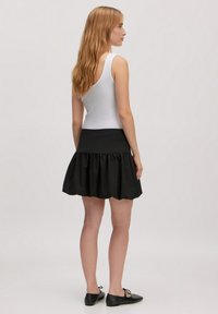 Zwarte flare rok met een gerimpelde zoom en een aansluitende tailleband, gecombineerd met een effen witte tanktop. Glad materiaal en eenvoudig ontwerp.