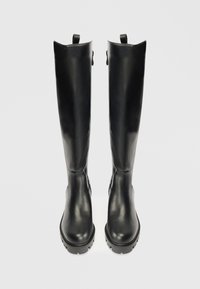 Botas de cuero negras hasta la rodilla con una textura suave, punta redondeada y suela resistente. Presenta dos lengüetas en la parte superior para facilitar su uso.