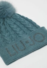 Beanie in maglia color turchese con un motivo a treccia e un pompon soffice sulla parte superiore. Presenta un risvolto con il testo "LIU·JO" decorato con strass.