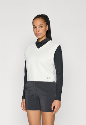 Top s výstřihem do V, zkrácený bezrukávový v světle šedé barvě s černým logem Nike, spárovaný s černými šortkami. Texturovaná tkanina se vrstveným designem.