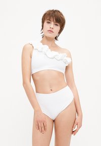 Biely bikiny set s textúrovaným topom na jedno rameno a volánikovým detailom, spolu s vysokým pásom. Jednoduchý, čistý dizajn.