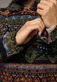 Fleece pullover met een gestructureerd oppervlak, voorzien van groene, zwarte, oranje en blauwe patronen, en een knoopsluiting aan de kraag met geribbelde boorden.
