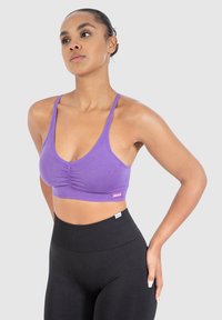 Väriä ribbattu violetti lyhyt toppi, jossa on rypistetty etuosa, ohuet hihnat ja logotieto, yhdistettynä korkeavyötäröisiin mustiin leggareihin.