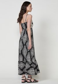 Robe maxi noire avec un motif paisley blanc, bretelles spaghetti et ourlet froncé. Associée à des sandales noires à brides.