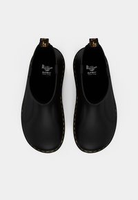 Zapatos negros sin cordones con un acabado suave, costuras amarillas a lo largo de la suela y una pestaña en el talón. Marca SoftWear en la plantilla.
